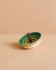 The Mader UFO Flora Spinning Top - Green, crafted from maple wood with green concentric circles and a brown handle, is displayed on a beige surface against a light beige background.