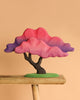 The Bumbu Handmade Wooden Japanese Maple Tree, with pink and purple layered foliage, is displayed on a wooden stool against a plain beige background.