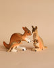 Three kangaroo figurines from the Bumbu Wooden Kangaroo Family Set, crafted from sustainably sourced wood, are arranged on a beige background—two adults face each other while a smaller kangaroo stands in front, inspiring imaginative play.