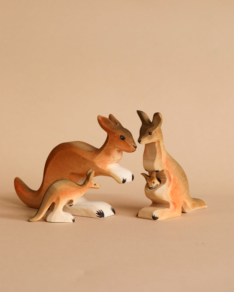 Three kangaroo figurines from the Bumbu Wooden Kangaroo Family Set, crafted from sustainably sourced wood, are arranged on a beige background—two adults face each other while a smaller kangaroo stands in front, inspiring imaginative play.