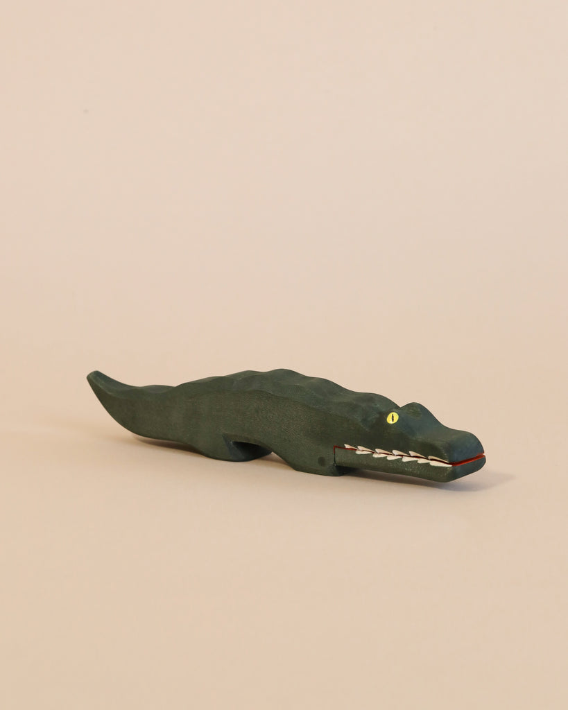 A dark green Ostheimer Crocodile with painted white teeth and yellow eyes, displayed on a plain light beige background.