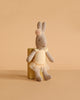 A Maileg Rabbit, Micro - Ballet Suit and Skirt, Cream (ships in one week), poses on a small yellow block against a beige background, resembling an adorable ballerina ready for the stage.
