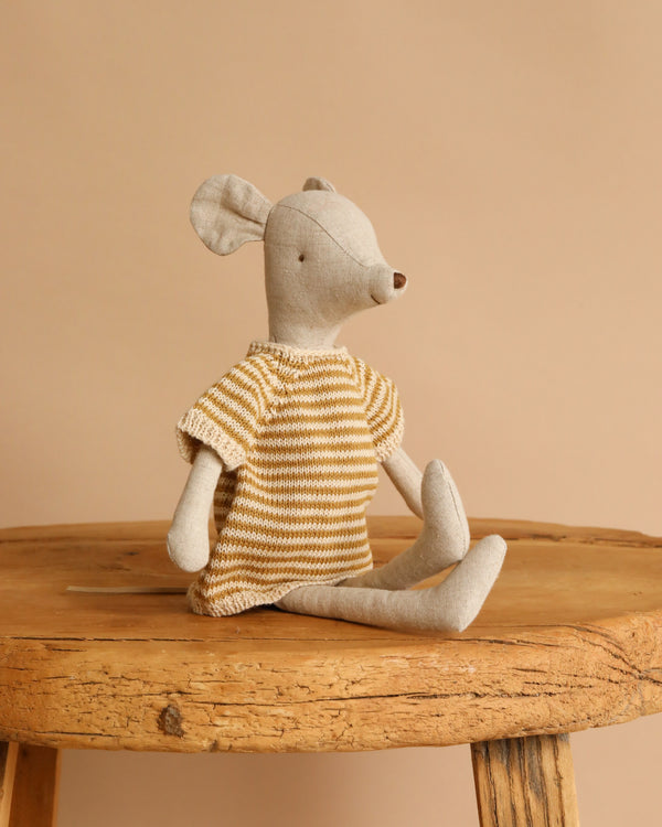 The Maileg Medium Mouse With Knitted Dress wears a yellow and white striped dress and sits on a rustic wooden stool in front of a plain beige background.
