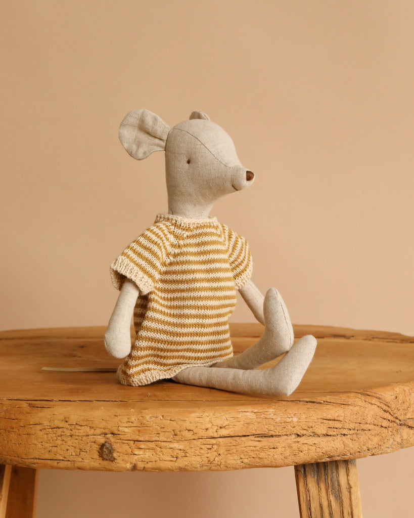 The Maileg Medium Mouse With Knitted Dress wears a yellow and white striped dress and sits on a rustic wooden stool in front of a plain beige background.
