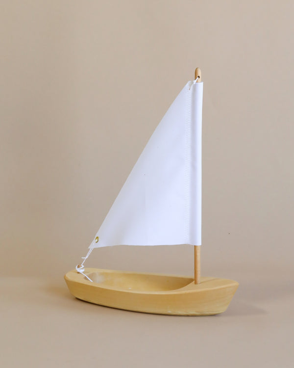 The Handmade Wooden Sailboat, crafted from lime wood with a white triangular sail, stands upright on a beige background—ideal for children aged 3 and up.