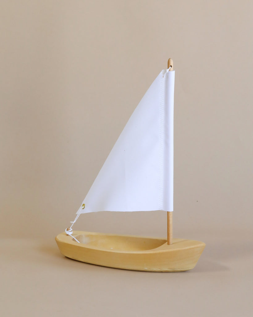 The Handmade Wooden Sailboat, crafted from lime wood with a white triangular sail, stands upright on a beige background—ideal for children aged 3 and up.