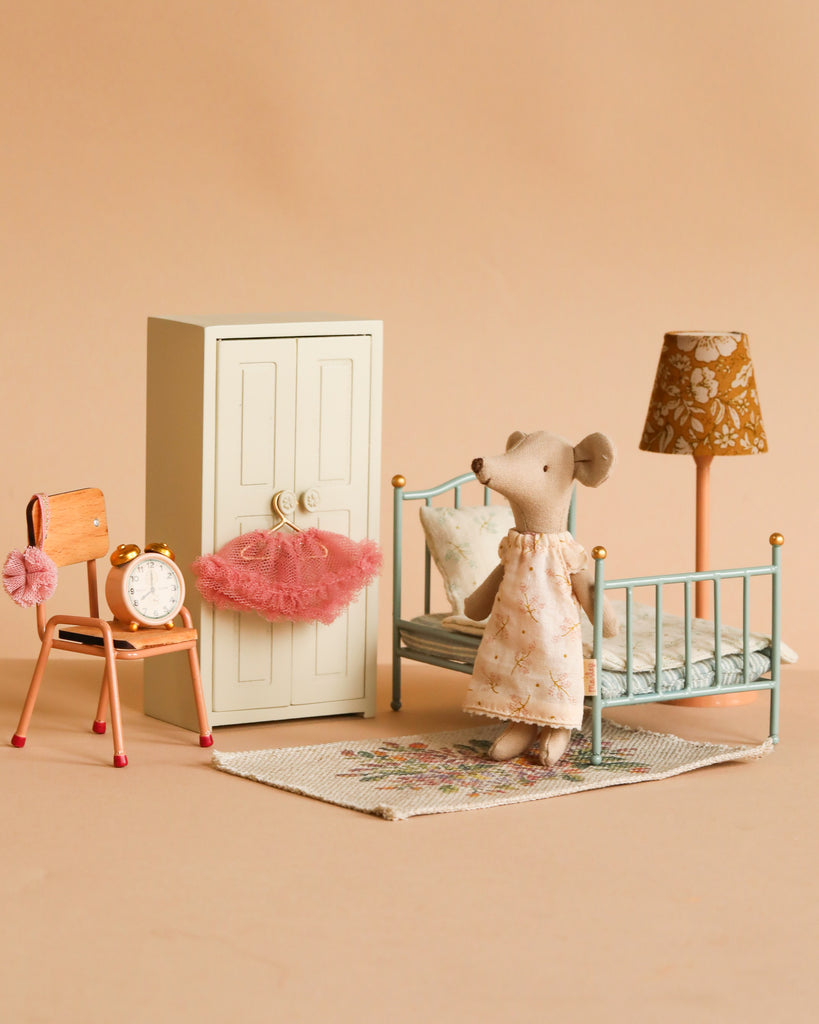 The Maileg Little Sister Bedroom Set features a Ballerina Mouse in a dress by a blue bed, wardrobe with pink tutu, chair with Maileg Alarm Clock, and Vintage Floor Lamp—all arranged on a beige background.