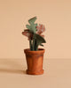 A small terracotta pot with a handmade fabric plant, featuring green and patterned leaves, complements the Maileg Dancing Mouse in Daybed – Cozy Morning Set, styled on a plain beige background.