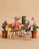 Two Maileg mice from the Picnic in the Garden Set wear red and blue striped shirts and sit at a small table with food, drinks, and potted plants, creating a cozy, playful scene.