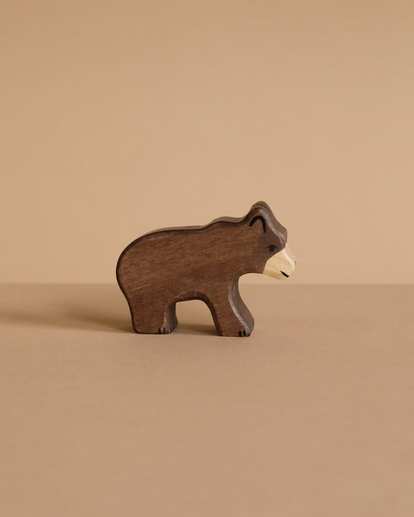 The Holztiger Small Brown Bear, a handcrafted wooden figurine, stands on a light brown surface against a matching beige background.