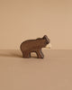 The Holztiger Small Brown Bear, a handcrafted wooden figurine, stands on a light brown surface against a matching beige background.