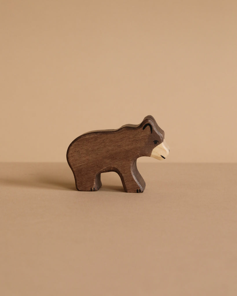 The Holztiger Small Brown Bear, a handcrafted wooden figurine, stands on a light brown surface against a matching beige background.