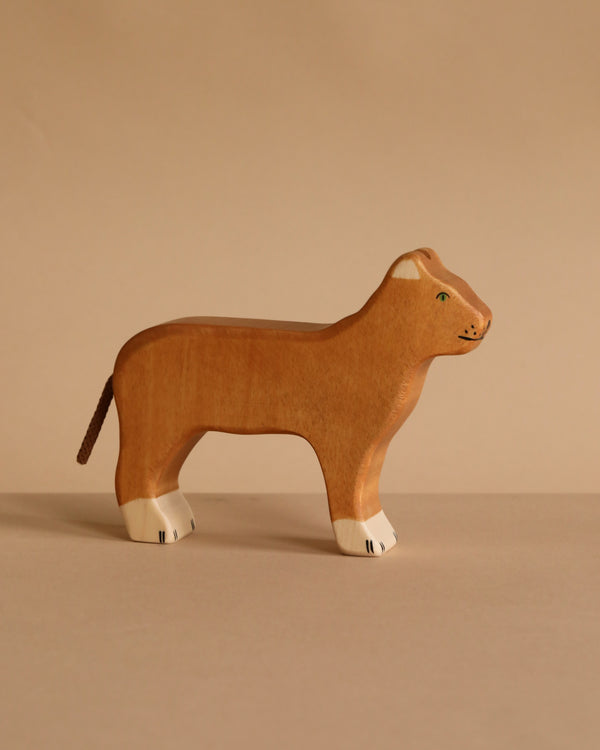 The Holztiger Lioness is a handcrafted wooden toy with painted facial features and white paw details, standing on a beige surface against a matching background. Part of the HOLZTIGER collection, it’s made in Europe.