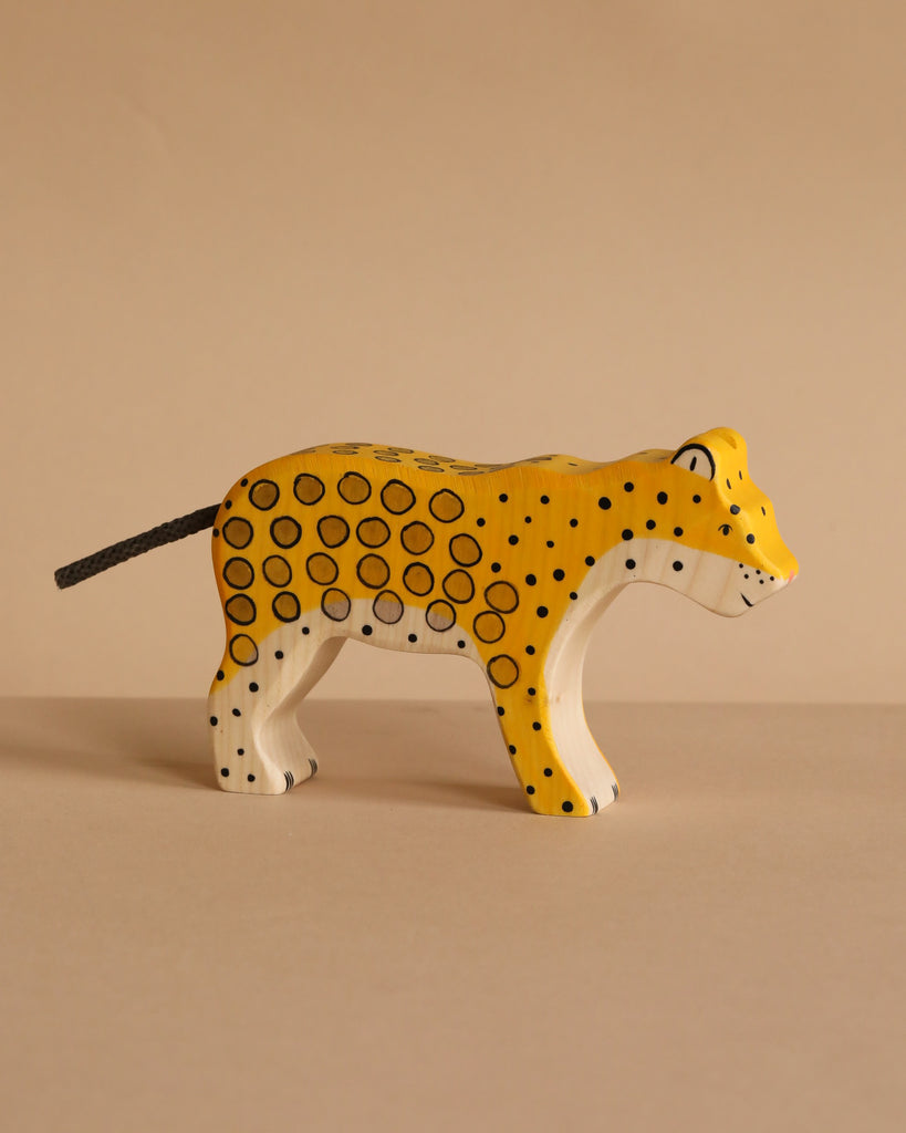 The Holztiger Leopard is a handcrafted wooden figure painted yellow with black spots and a white underside, shown standing on a beige surface against a beige background. Made in Europe.