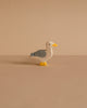 The Holztiger Seagull is a small, handcrafted wooden figurine featuring gray wings, a white head, yellow beak and feet. It stands on a plain beige surface with a matching background. Made in Europe by HOLZTIGER.