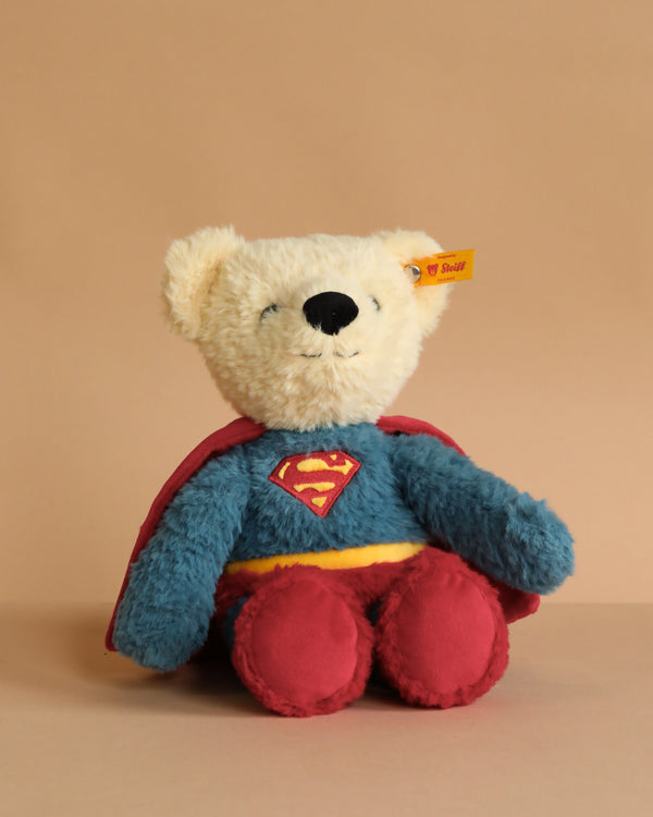 The Steiff Superman Teddy Bear, 12 Inches, features a plush bear in a blue and red Superman costume with cape and "S" logo, sitting upright against a beige background—perfect for superhero adventures.