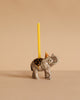 The Elephant Cake Topper features a porcelain elephant with a yellow candle on its back and an orange party hat, set against a beige background—an adorable collectible keepsake for any décor.