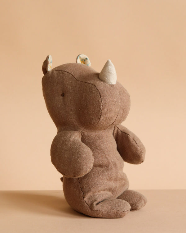 The Maileg Small Rhino - Chocolate, crafted from soft fabric and recycled polyester, sits upright on a neutral beige background—perfect for joining your Safari friends collection.