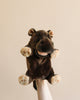 The Hippo Puppet, featuring a plush hand design, is showcased against a simple light grey backdrop. The puppet boasts a rich brown color with lighter beige accents on its feet, mouth, and nostrils. It also has plush ears, a wide mouth with a pink tongue, and small brown eyes that contribute to its charmingly realistic appearance.