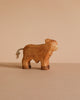 A small, handcrafted wooden toy named Handmade Wooden Highland Calf, made from sustainable hardwood with a minimalist design and short rope tail, is shown on a light brown surface against a beige background.