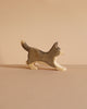 The Handmade Wooden Border Collie is a small, handcrafted dog figurine with a raised tail, painted in brown and beige plant-based stains. It stands on a light brown surface with a matching background.