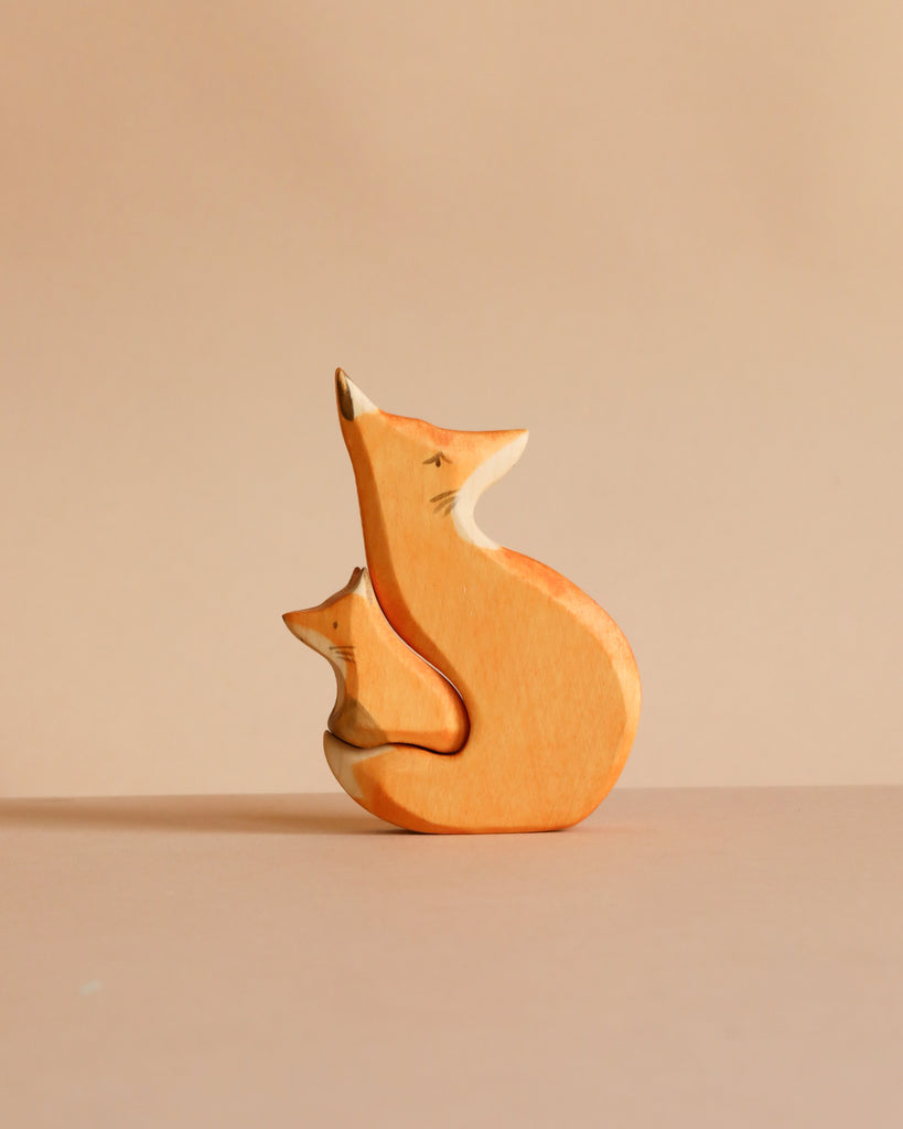 The Handmade Wooden Snuggling Foxes set features two minimalistic fox figurines, one large and one small, hand crafted from sustainable hardwood and finished with natural, non-toxic stains against a beige background.