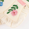 Close-up of Meri Meri Butterfly Wings in cream-colored natural cotton with ruffled edges, embroidered pink and blue flowers, green leaves, and a pink velvet ribbon accent.