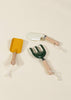 The Gardening Tools Playset features three kids' tools with light wooden handles and white cord loops—a yellow trowel, a white trowel, and a green hand rake—arranged on a beige background, ideal for educational play.