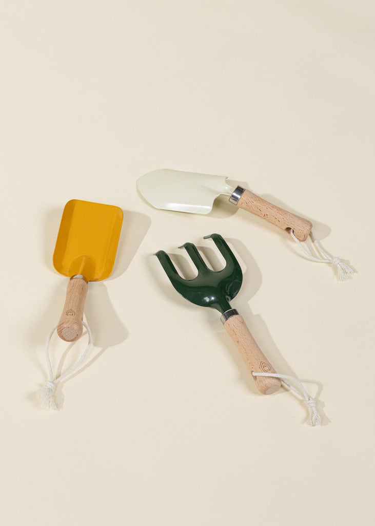The Gardening Tools Playset features three kids' tools with light wooden handles and white cord loops—a yellow trowel, a white trowel, and a green hand rake—arranged on a beige background, ideal for educational play.