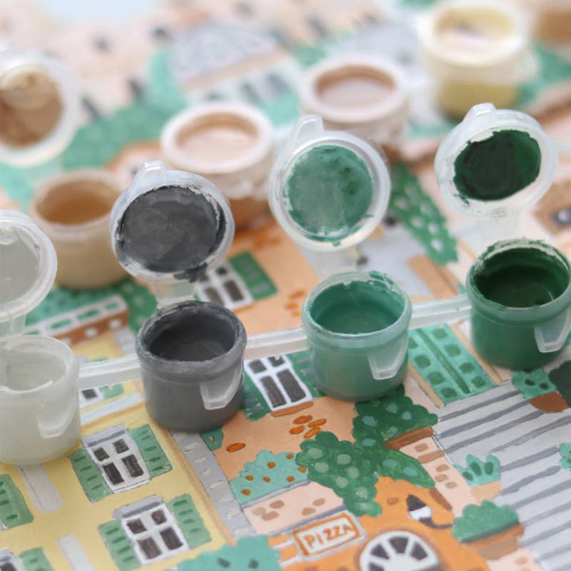 Small open paint pots in white, gray, green, and brown are arranged on a cityscape—perfect for aspiring artists to spark creativity with the Paint By Number Kit - Rome.