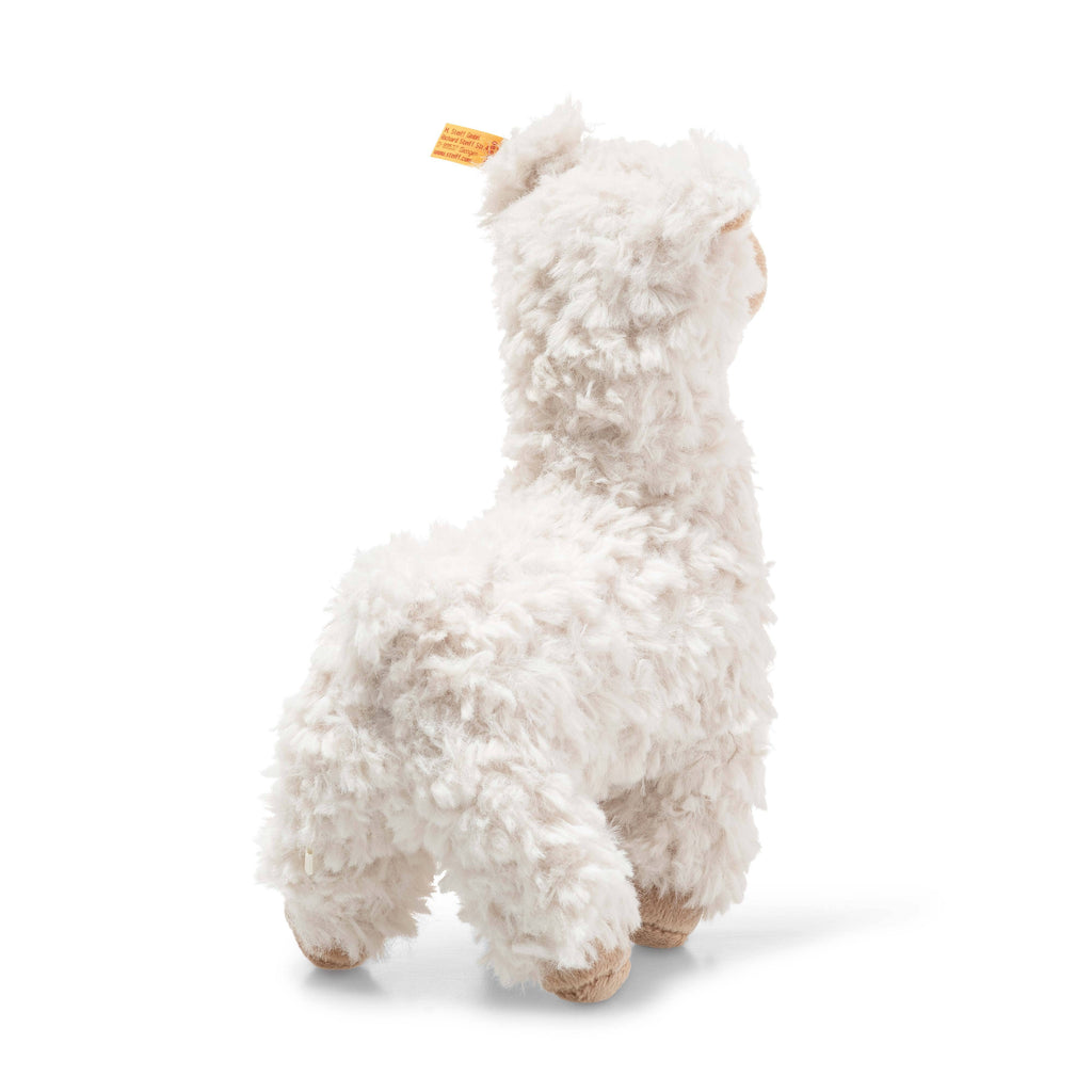 The Steiff Leandro Llama Plush Toy, 7 Inches, has soft white textured fur, stands on all four legs with a small yellow tag on its ear, and is perfect for cuddly friends. The background is plain white.