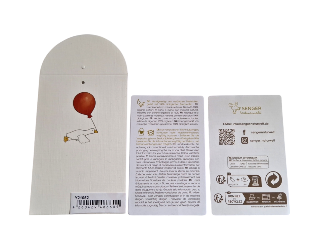 Three tags: the left shows a red balloon held by the Senger Naturwelt Cuddly Animal - Dolphin’s flipper, the middle details GOTS-certification in German, and the right features logo, contact info, social icons, and recycling symbols.
