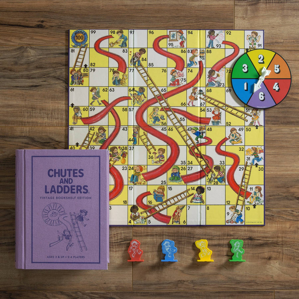 The Chutes and Ladders Vintage Bookshelf Edition is shown on a wooden surface with its purple box, four colorful player pieces, a spinner, and the illustrated board featuring ladders and slides.