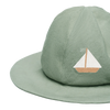 The Donsje Organic Cotton Steijn Boat Hat is light green with a wide brim and features an embroidered sailboat with a white sail and tan hull on the front, offering stylish sun protection.