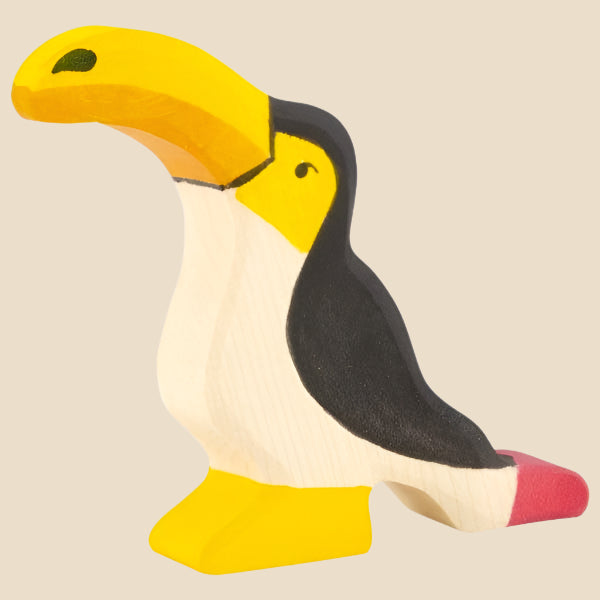 The Holztiger Toucan, handcrafted from maple and beech wood, features a yellow beak and foot, black back, white belly, and a pink tail detail—shown in classic HOLZTIGER style against a light beige background. Ships in one week.