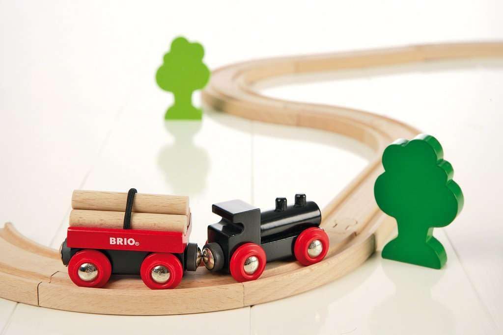 The BRIO Little Forest Train Set features a wooden toy train with a black engine, red log car, curved track, and two green tree figures—ideal for any BRIO collection or as a delightful train starter set.