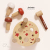 The Woodland Mushroom Hammer Game features a round base with autumn leaf and acorn designs, four smiling mushroom pegs in brown, red, and white, and a wooden mallet—perfect for building fine motor skills.