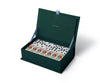 The Strawberry Fields Dominoes Set features open dark green dominoes with classic black dots and some with vibrant illustrated designs. The inside lid displays gold text reading "Rifle Paper Co.