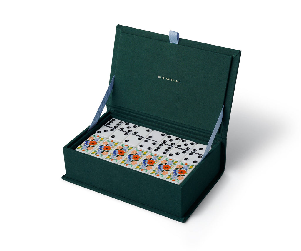 The Strawberry Fields Dominoes Set features open dark green dominoes with classic black dots and some with vibrant illustrated designs. The inside lid displays gold text reading "Rifle Paper Co.