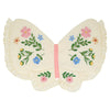 The Meri Meri Butterfly Wings pillow features a butterfly shape in cream natural cotton with ruffled edges, colorful embroidered flowers and green leaves on the wings, and a pink stripe at the center resembling a butterfly's body.