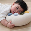 A baby rests on a wooden floor, their head on the Tummy Time Palette—a round pillow featuring five colorful, textured circles. The baby gazes ahead, looking relaxed and comfortable with this cozy nursery accessory.