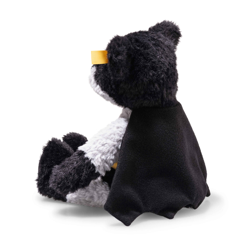 The Steiff Batman Teddy Bear, 12 Inches, sits upright with a black cape and yellow mask over its eyes, resembling the iconic superhero. The plush panda is set against a plain white background.