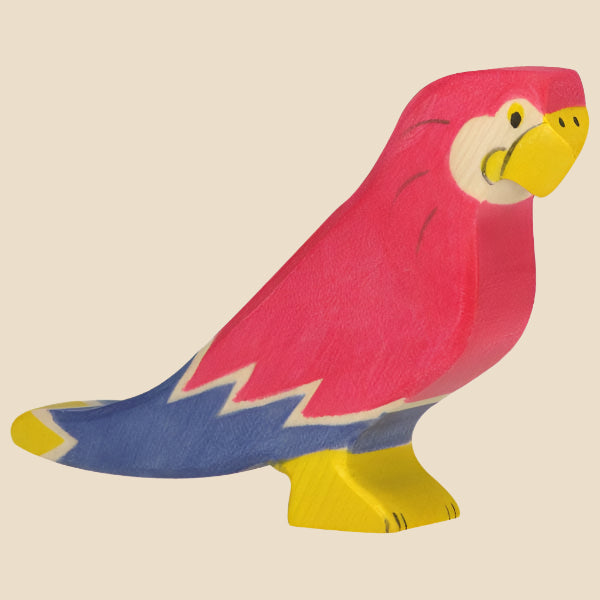 The Holztiger Parrot is a colorful handcrafted wood figurine with a pink body, yellow beak and feet, white and yellow accents, and blue tail. Made in Europe as part of the HOLZTIGER collection; ships in one week. Shown on a light background.