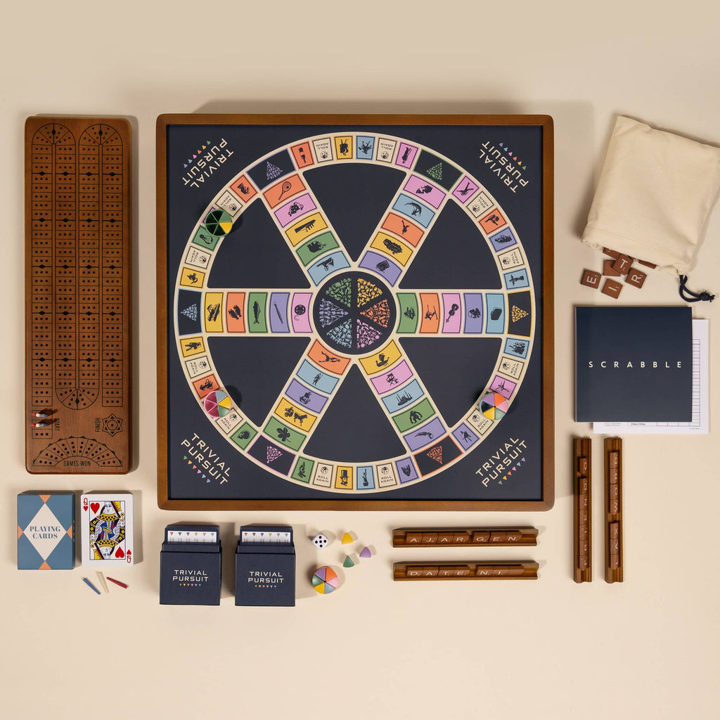 A flat lay featuring the 3-in-1 Game Collection: Scrabble with letter racks and score pad, Trivial Pursuit board with cards, pie pieces, dice, and Cribbage board with pegs—all together in one set.