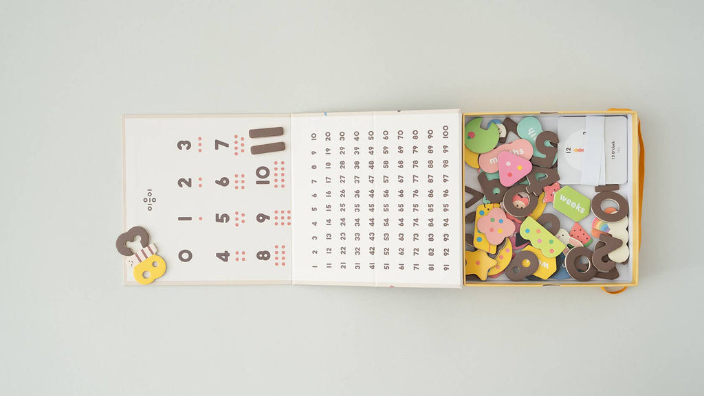 An open Magnetic Number Play Set displays a calendar with numbers and symbols on the left and colorful magnetic wooden pieces shaped like animals, objects, and alphabet cards on the right.