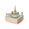The Paris Music Box features a classic design with miniature models of the Eiffel Tower, a bridge, lamp post, trees, and a boat on a blue river.