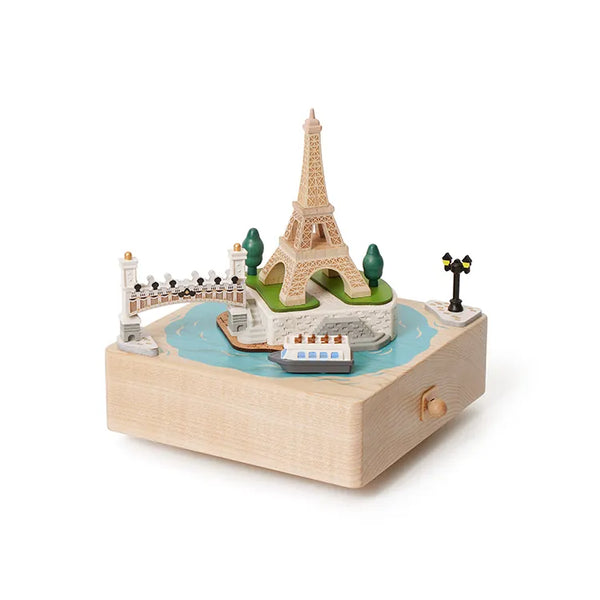 The Paris Music Box features a classic design with miniature models of the Eiffel Tower, a bridge, lamp post, trees, and a boat on a blue river.
