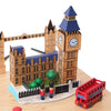 The London Music Box is a decorative wooden set featuring models of Big Ben, nearby buildings, two toy soldiers, green trees, and a red double-decker London bus all displayed on a wooden base.