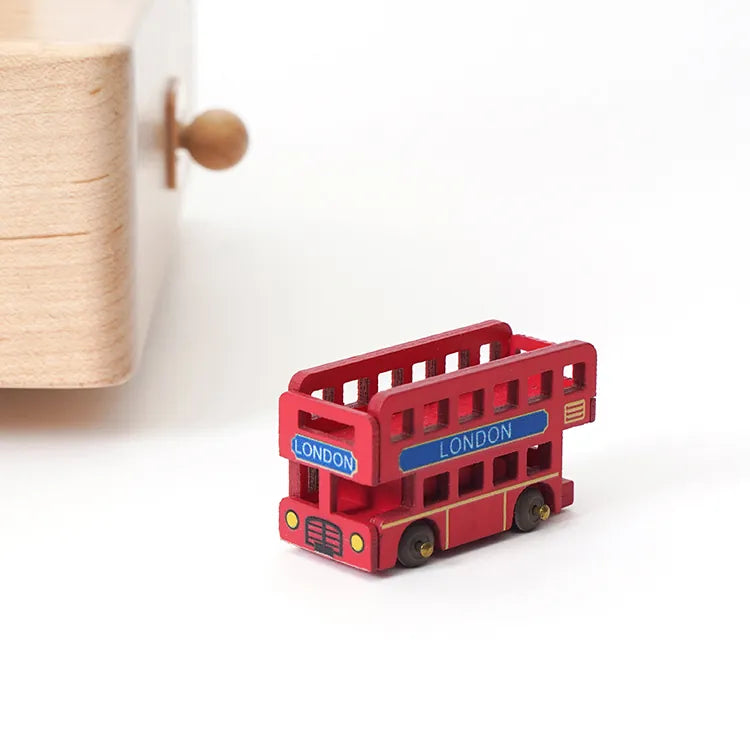 A London Music Box with a round wooden knob sits on a white surface, next to a small red toy double-decker bus marked "London.