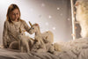 A young girl in pajamas sits on a bed with four unicorn plush toys, including the 11-inch Steiff Unica Unicorn Stuffed Plush Toy. Soft lighting and decorative stars create a cozy, whimsical atmosphere inspired by this beloved fantasy animal.